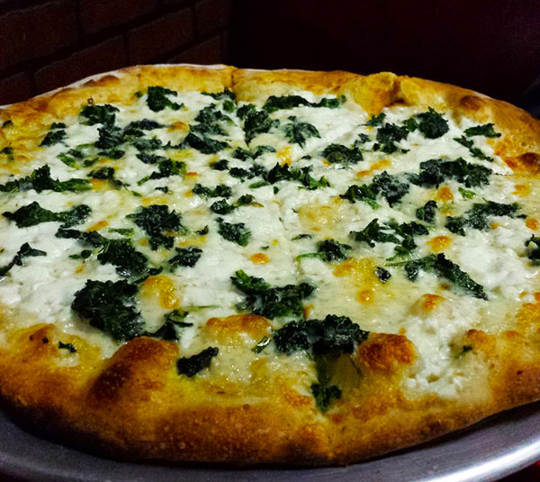 A freshly baked spinach and cheese pizza, sliced and served on a metal tray.