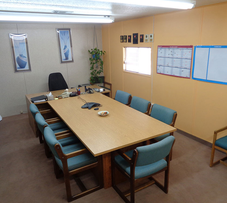 Conference room with a rectangular table, blue chairs, wall calendars, and framed art on beige walls.