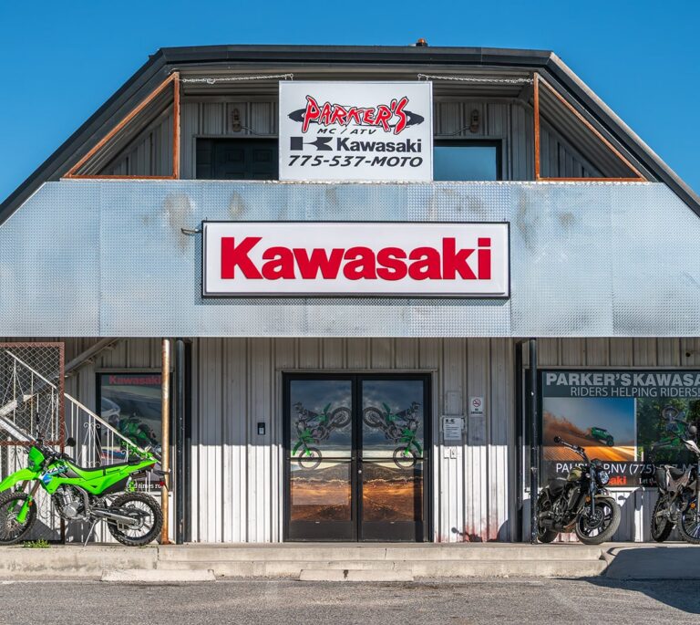 Front view of a Kawasaki dealership with motorcycles displayed outside and a large Kawasaki sign above the entrance.