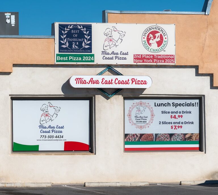 Storefront of MiaAua East Coast Pizza with signs for awards and lunch specials on a beige building.