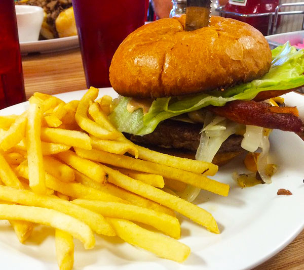 A plate with French fries and a cheeseburger topped with lettuce, bacon, and onions.