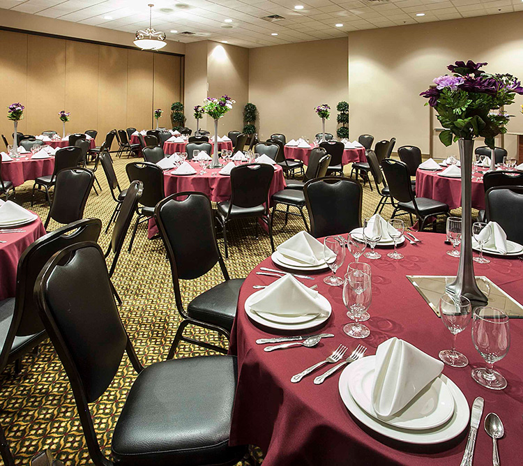 Banquet hall with round tables set with maroon tablecloths, napkins, glassware, and floral centerpieces.