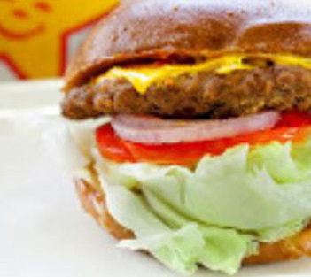 A close-up of a hamburger with lettuce, tomato, onion, cheese, and a beef patty in a bun.