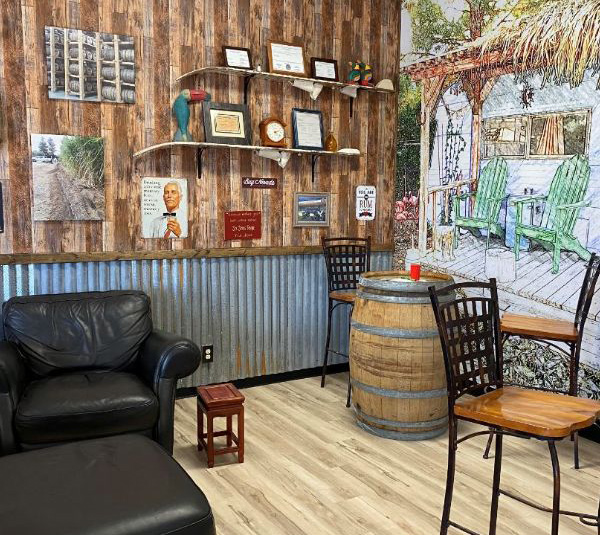 Cozy rustic room with leather chairs, barrel table, wood-paneled walls, and eclectic wall decor.
