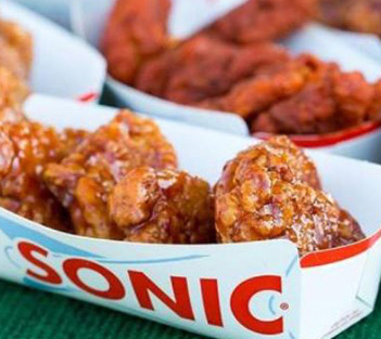 Chicken wings with sauce served in a paper tray with the SONIC logo at a restaurant.