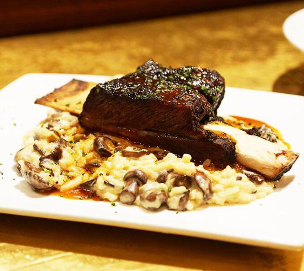 Braised beef short rib on creamy mushroom risotto, garnished with herbs, served on a white plate.