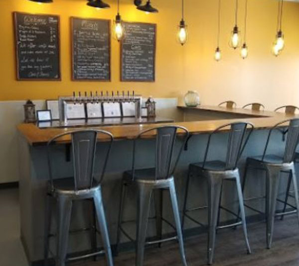 Bar counter with metal stools, hanging lights, and menu boards on a yellow wall.