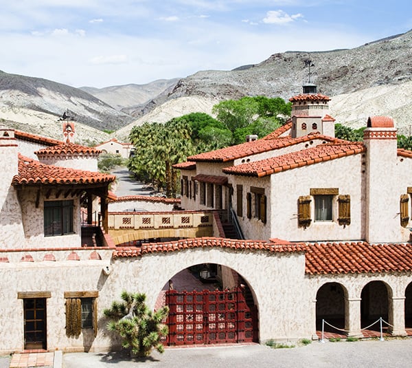 Spanish-style villa with red tile roofs, surrounded by mountains and desert landscape under a clear sky.