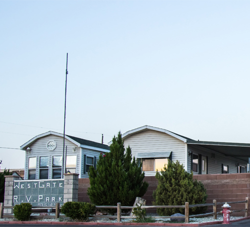 Two white mobile homes and a Westgate R.V. Park sign surrounded by bushes and a short fence.