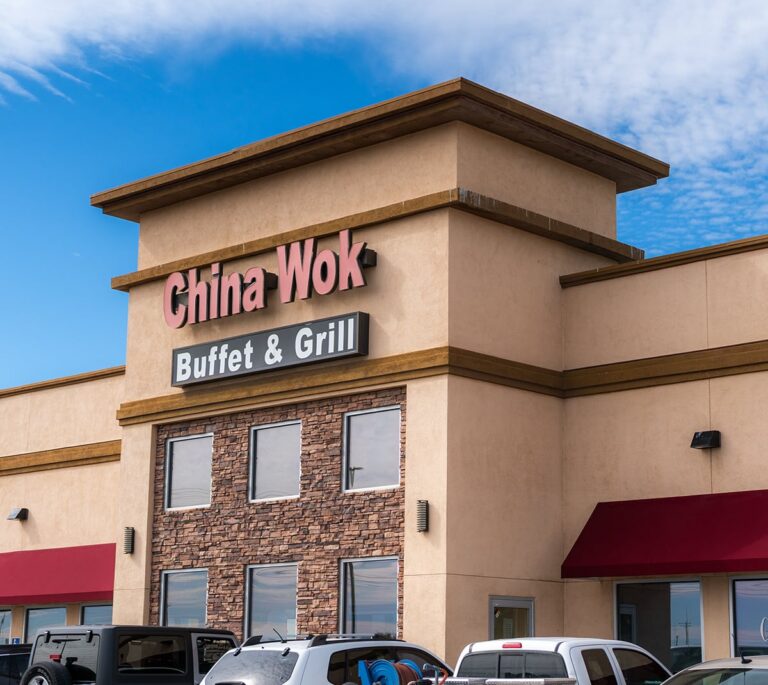 China Wok Buffet & Grill restaurant exterior with signs, windows, and parked cars under a blue sky.