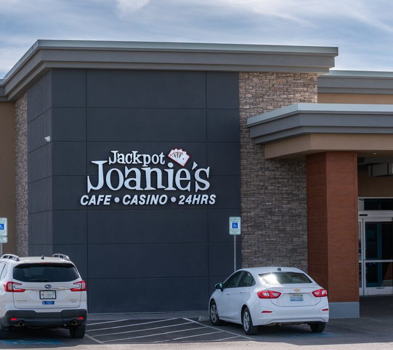 Exterior of Jackpot Joanie’s Cafe Casino with two parked cars and a sign showing it’s open 24 hours.
