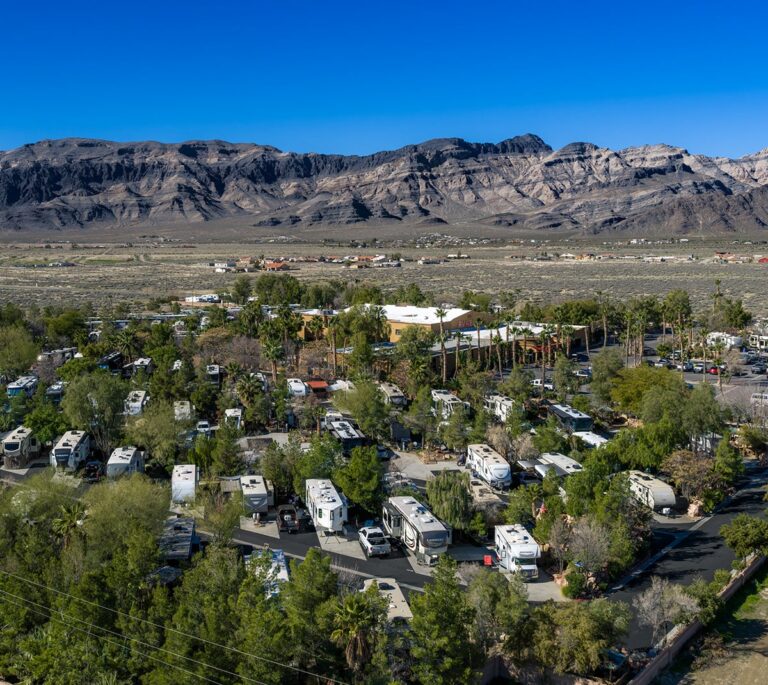 Aerial view of an RV park with many motorhomes, surrounded by desert landscape and mountains in the background.