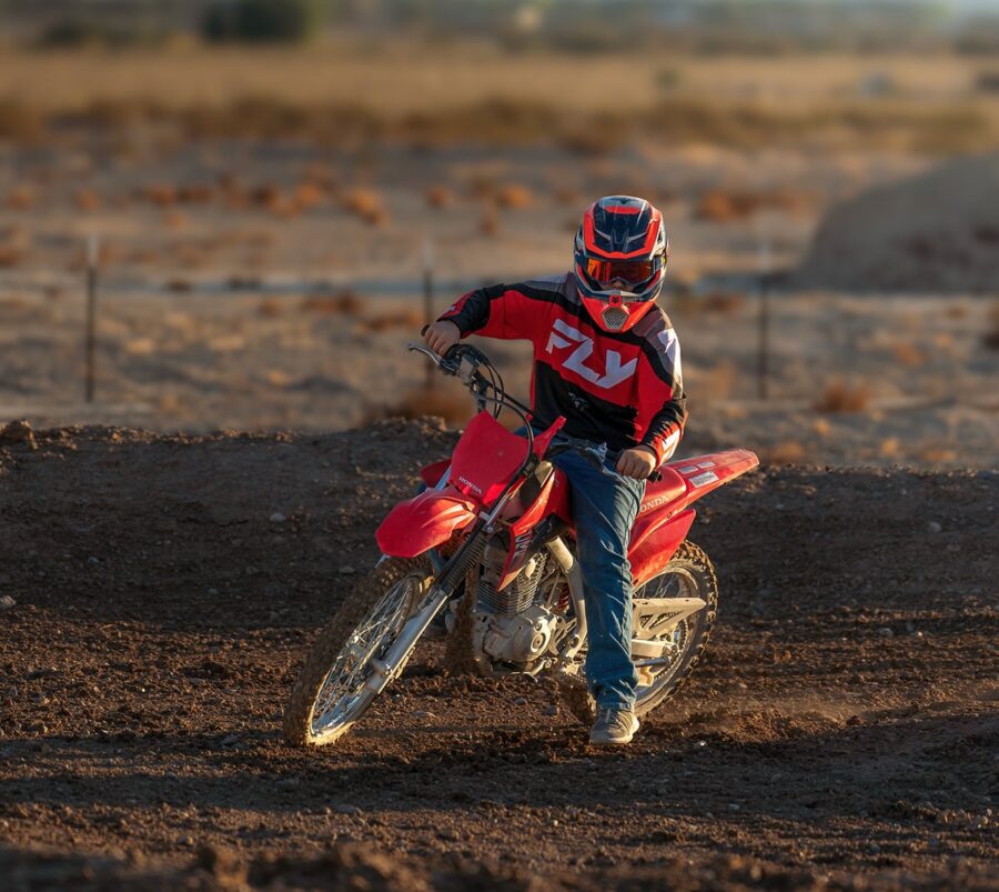 A person in motocross gear riding a red dirt bike on a dirt track in a desert landscape.