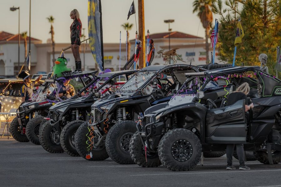 Row of decorated off-road vehicles in a parking lot, with people standing and sitting on them.