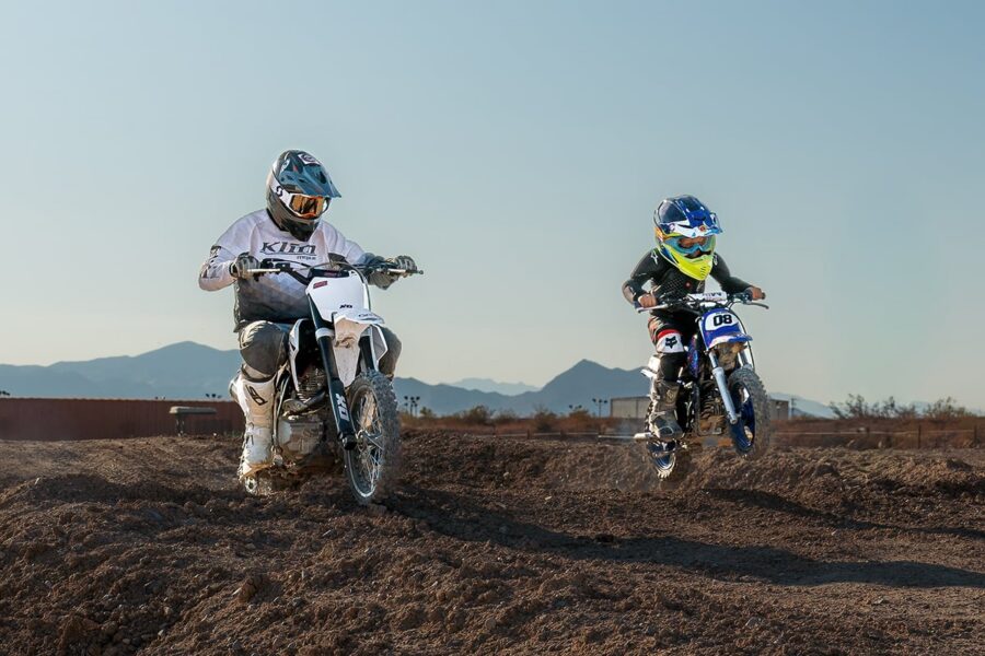 Two people riding dirt bikes off-road with mountains in the background under a clear sky.