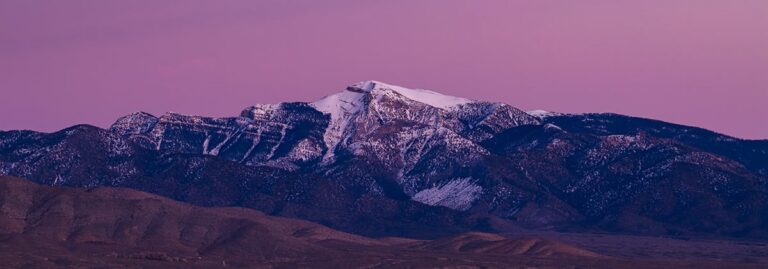 Snow-capped mountain peak at dusk with a purple sky in the background.