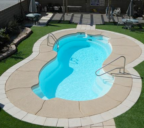 A small, kidney-shaped backyard swimming pool with clear blue water and metal handrails.
