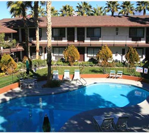 Outdoor swimming pool surrounded by lounge chairs, palm trees, and a two-story motel-style building.
