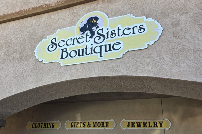 Secret Sisters Boutique sign above a store, offering clothing, gifts & more, and jewelry.