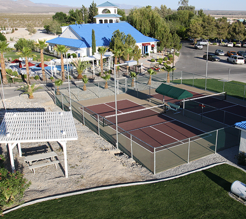 Aerial view of two outdoor fenced pickleball courts near a building with a blue roof and palm trees.