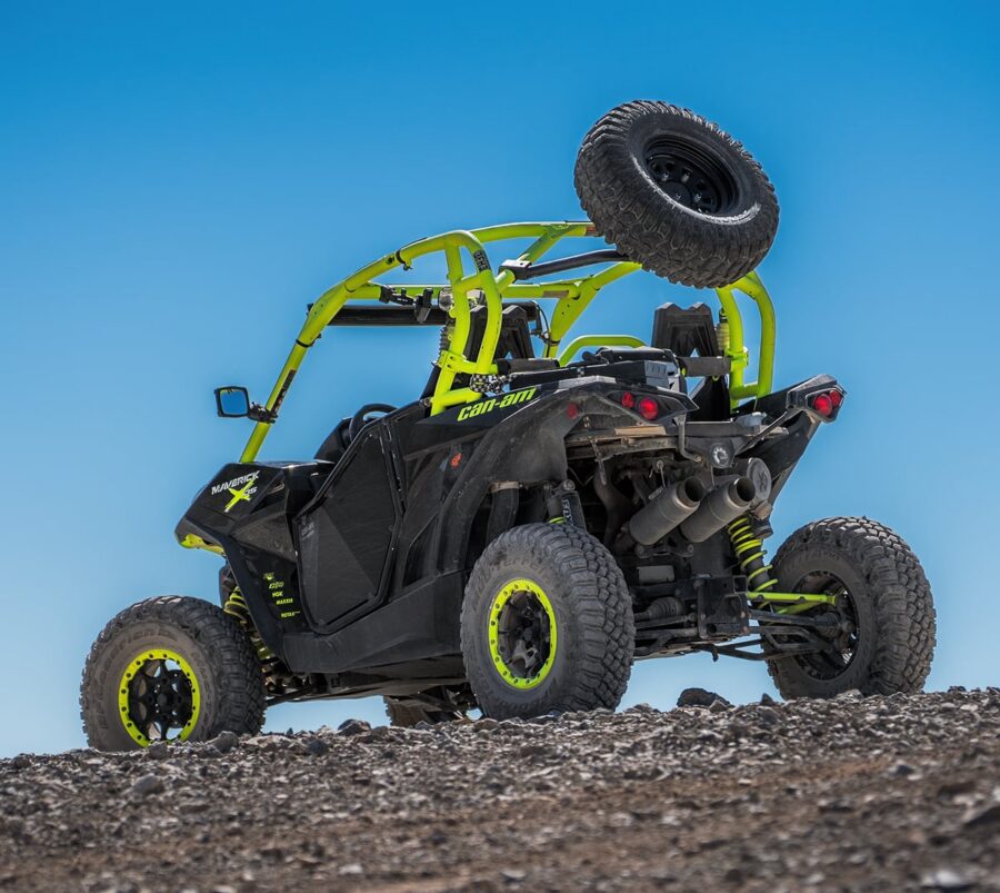 A black and neon green off-road ATV with a spare tire on top, parked on rocky terrain under a blue sky.
