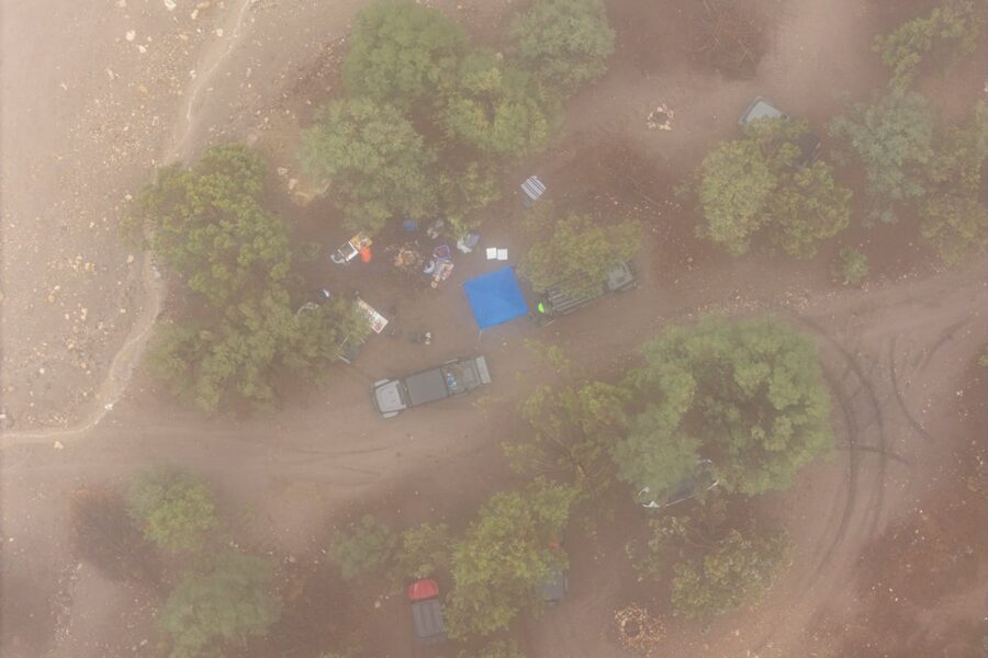 Aerial view of a campsite with tents, vehicles, and trees on a dirt clearing in foggy conditions.