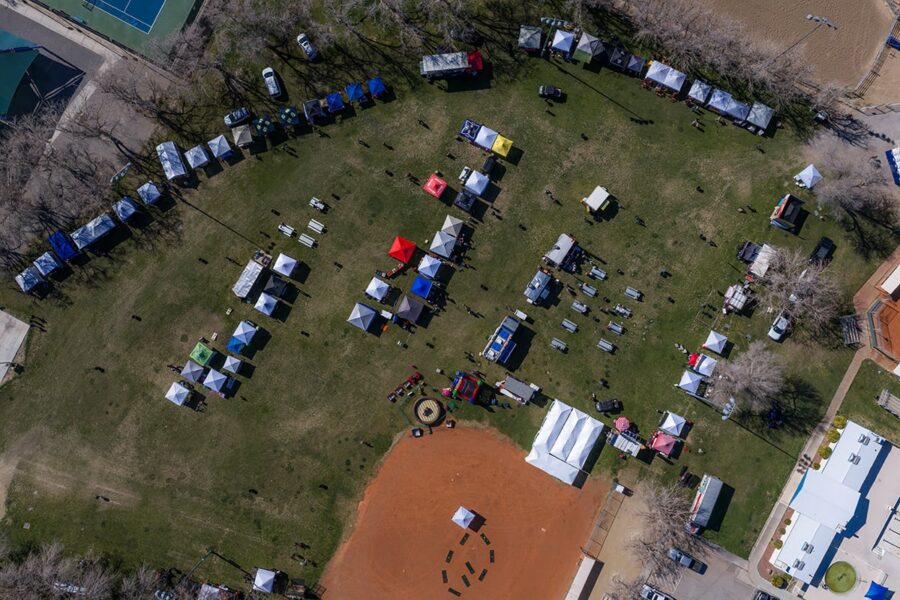 Aerial view of a park event with colorful tents, booths, and scattered people on a grassy field.