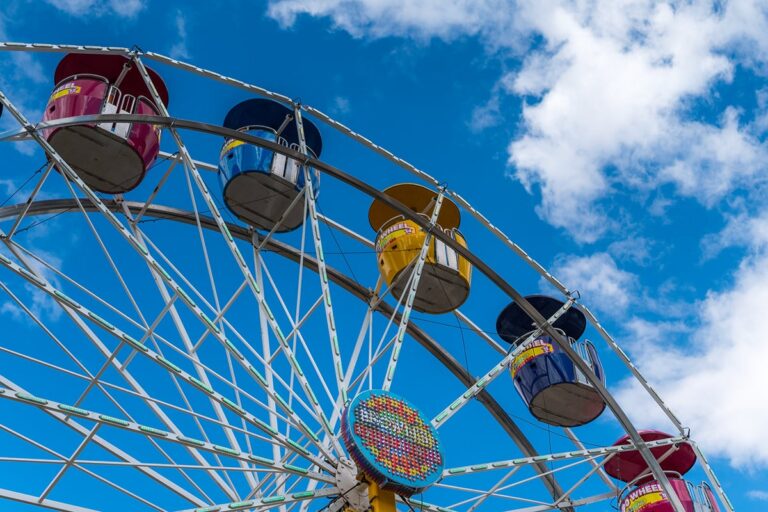 Colorful Ferris wheel against a bright blue sky with clouds, viewed from below.