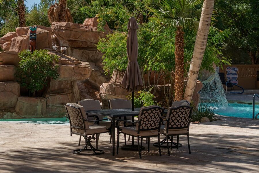 Outdoor patio table and chairs by a pool, with rocks, trees, and a waterfall in the background.
