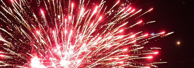 Bright red and white fireworks explode against a dark night sky.