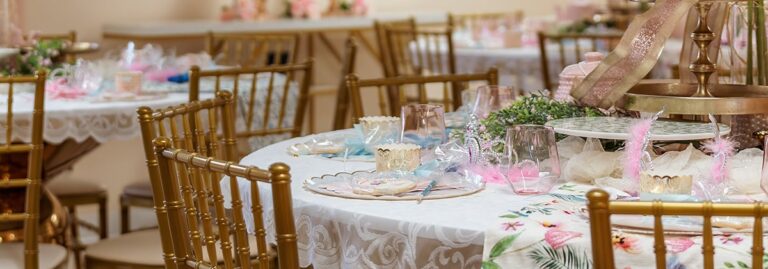Round tables with white lace cloths, gold chairs, and pastel party decor set for a celebration.