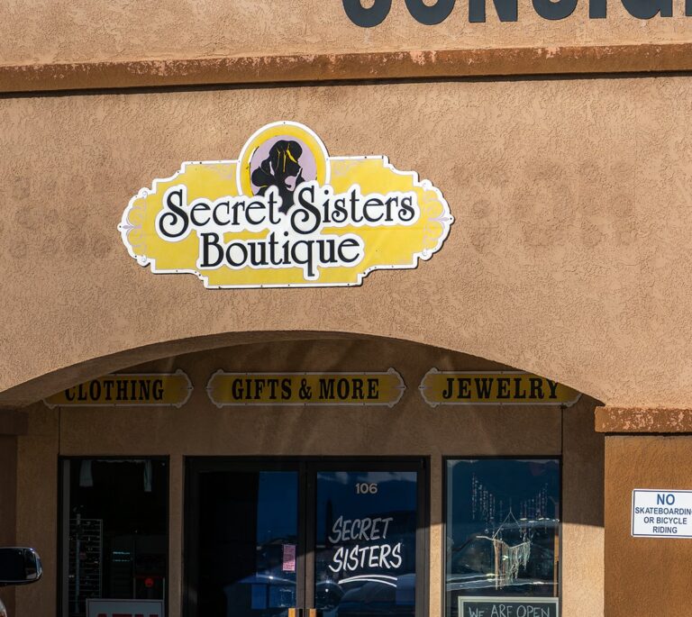 Storefront of “Secret Sisters Boutique” with signs for clothing, gifts, jewelry, and a “No Skateboarding” notice.