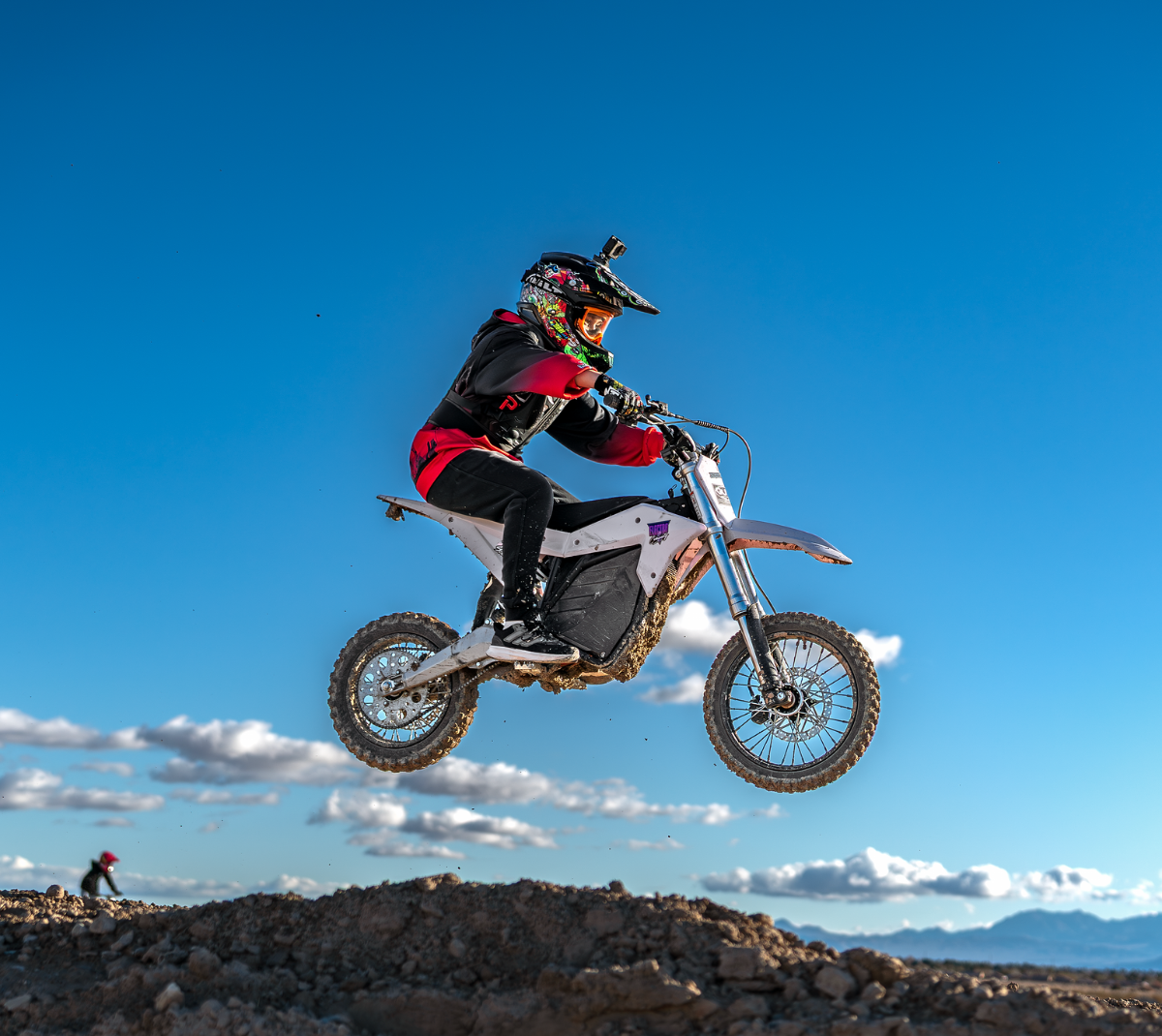 A motocross rider in mid-air on a dirt bike, jumping over rocky terrain under a clear blue sky.