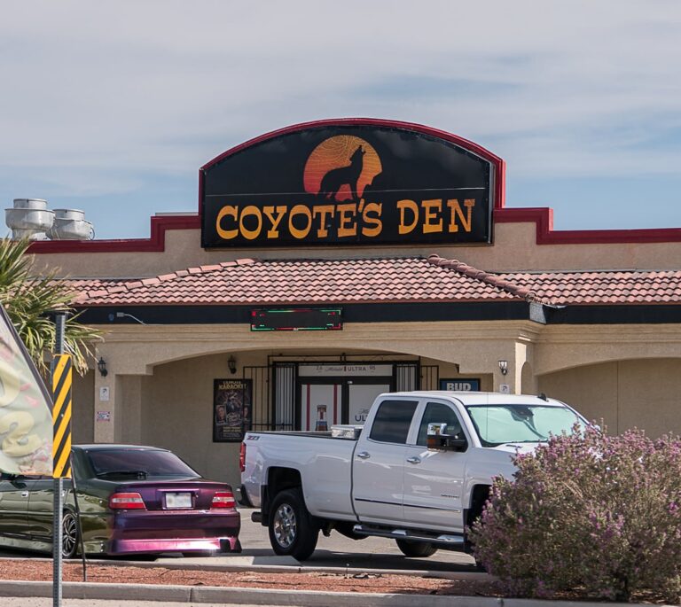 Exterior of Coyotes Den restaurant with a white pickup truck and a purple car parked in front.