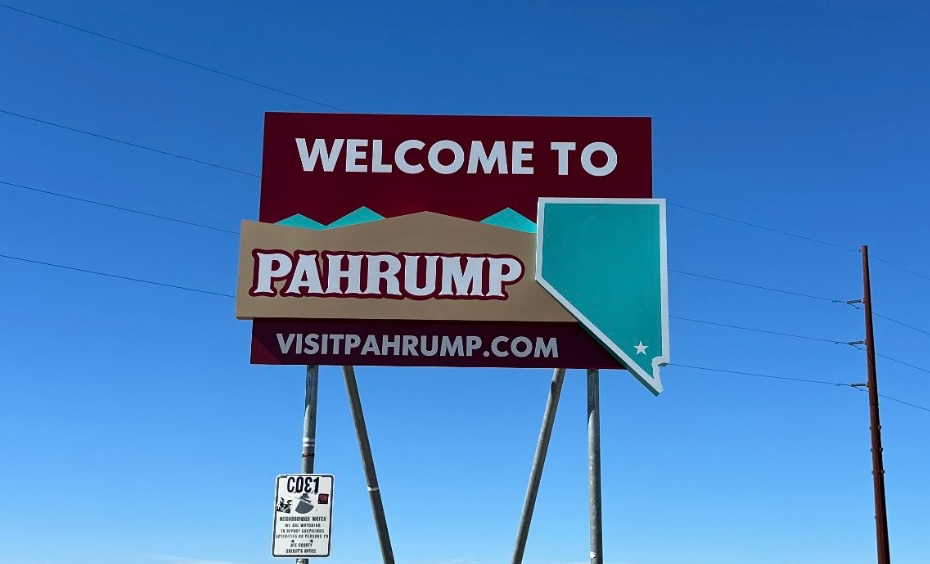 Large roadside sign reads Welcome to Pahrump, visitpahrump.com against a clear blue sky.