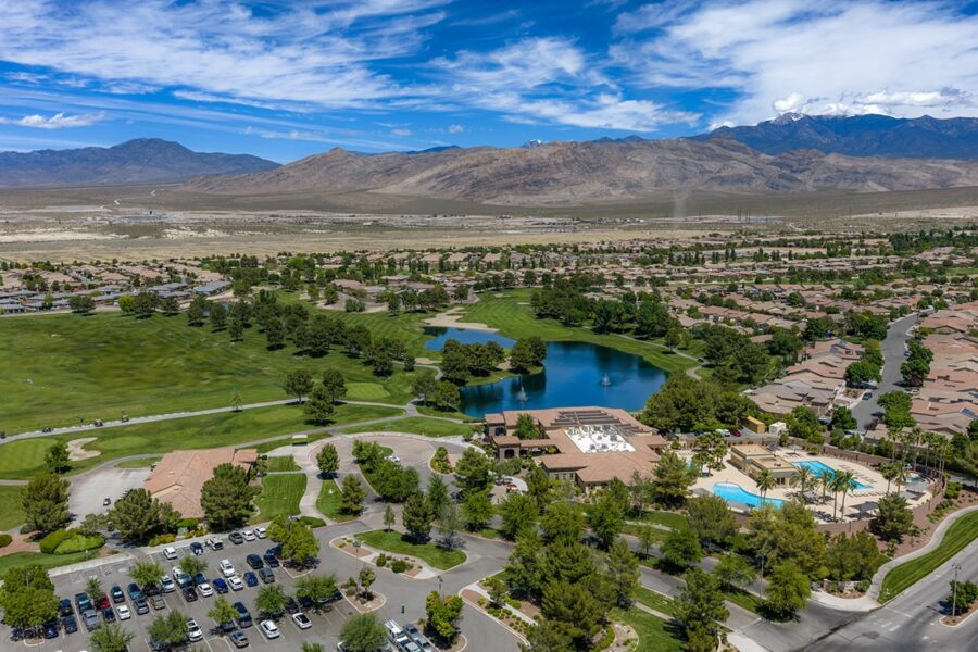Aerial view of a suburban neighborhood with a golf course, lake, pool, and mountains in the background.