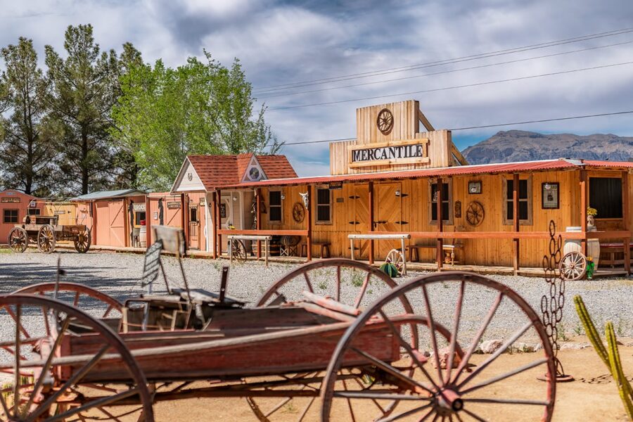 Old Western-style wooden buildings with a mercantile store and antique wagon in the foreground.