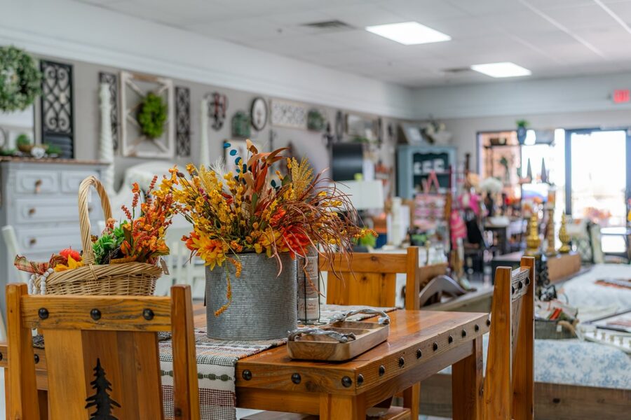 Wood table with fall floral centerpiece in a home decor store, surrounded by rustic furnishings and wall art.
