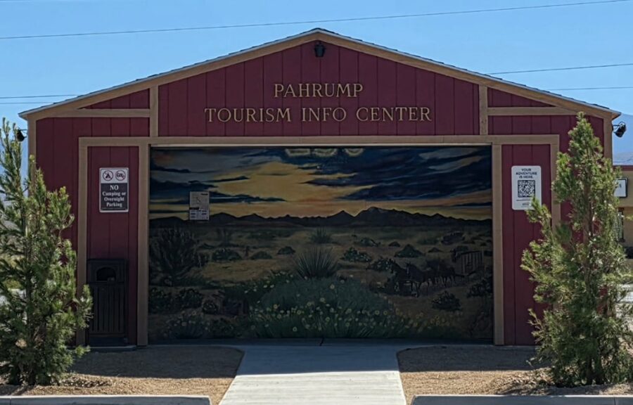 Red building labeled Pahrump Tourism Info Center with a desert mural and QR code signs by the entrance.