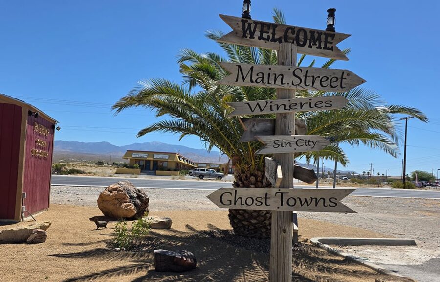 Wooden signpost with arrows points to Main Street, Wineries, Sin City, and Ghost Towns in a desert setting.