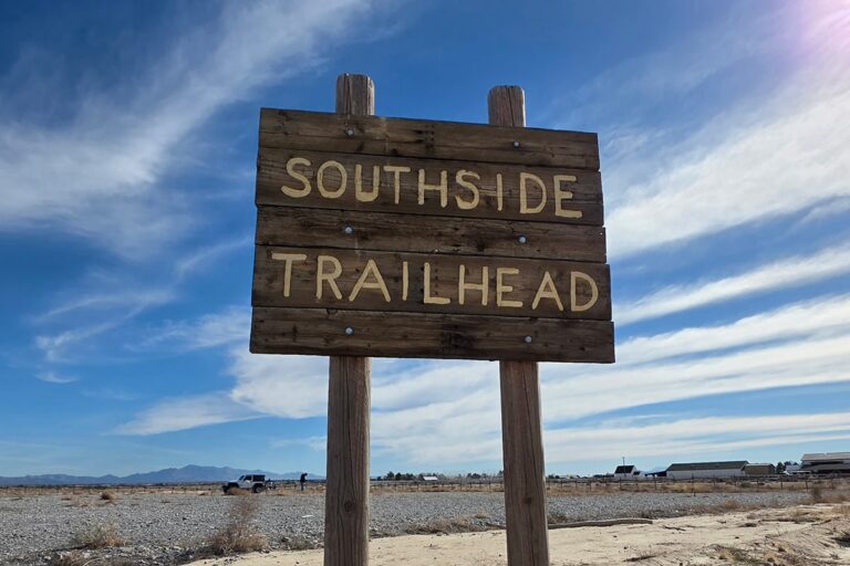 Wooden sign reads Southside Trailhead with blue sky, clouds, and a few vehicles in the background.