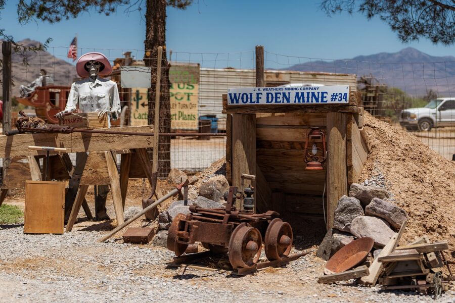 A wooden Wolf Den Mine entrance with old mining tools and a mannequin dressed as a miner nearby.