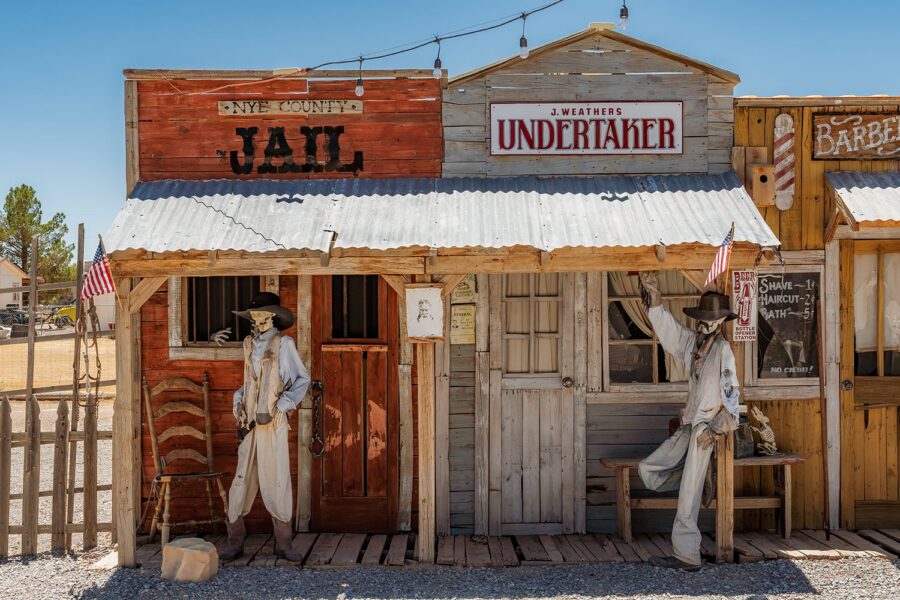 Old western jail and undertaker buildings with two cowboy mannequins and rustic decor in bright sunlight.