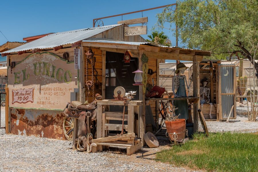 Weathered wooden shack with a sign, rustic decor, and skeletons displayed outside on a sunny day.