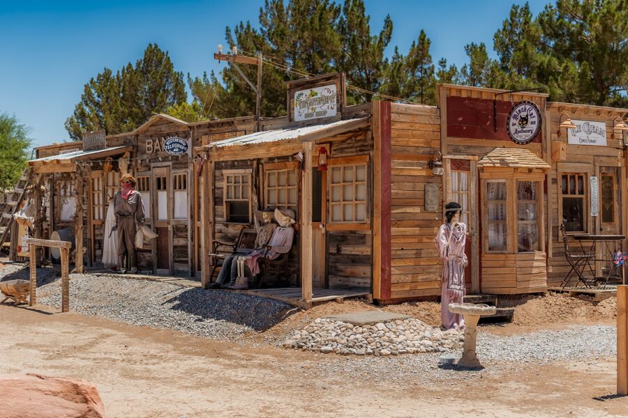 Old Western town buildings with mannequins dressed in period clothing standing and sitting outside.