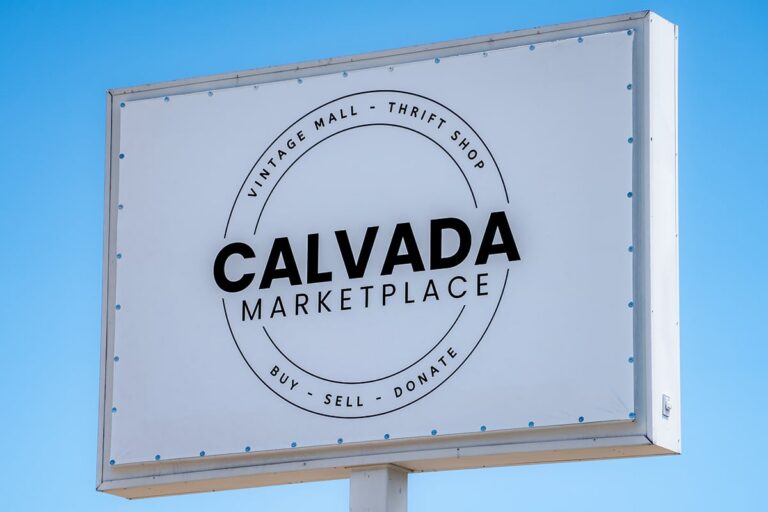 White sign reading Calvada Marketplace, Vintage Mall - Thrift Shop, Buy - Sell - Donate against blue sky.