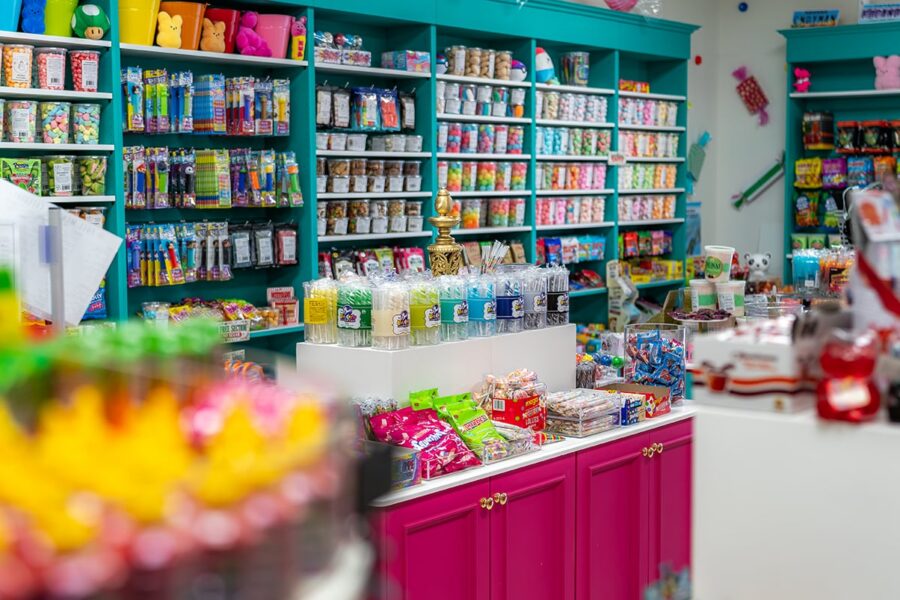 Colorful candy store with shelves full of sweets, snacks, and drinks, plus treats displayed on a central table.