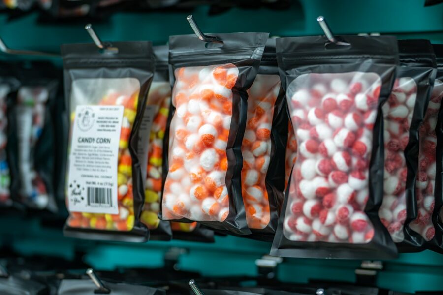 Clear bags of colorful candy, including orange and white, hang on hooks against a teal background.