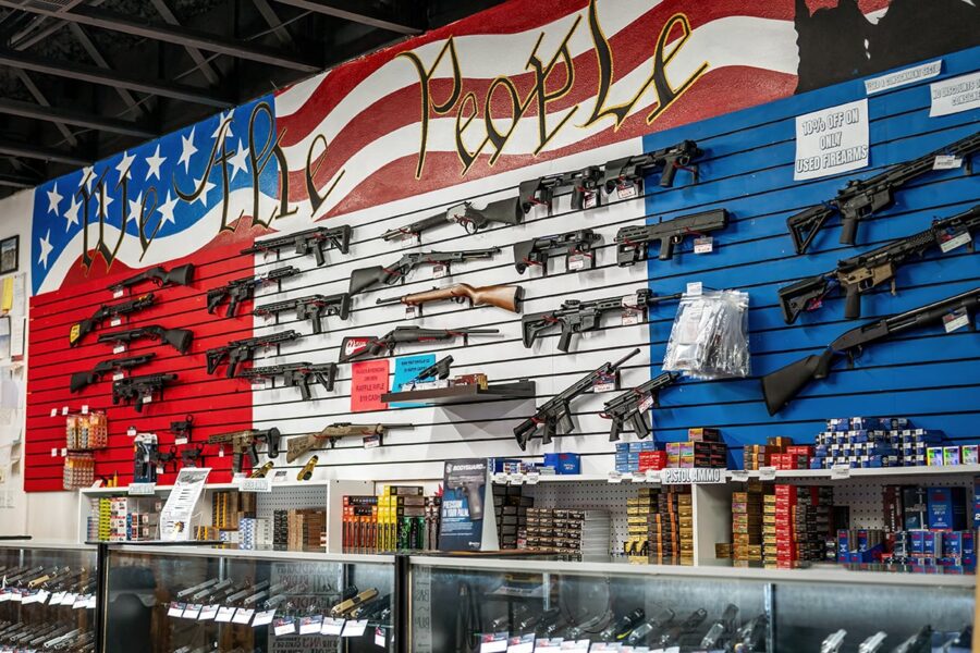 Rifles and ammunition displayed on a wall painted as an American flag with We the People text.