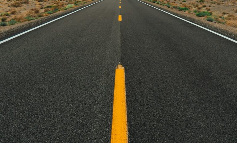 A straight, empty road with a yellow centerline stretches into the desert landscape.